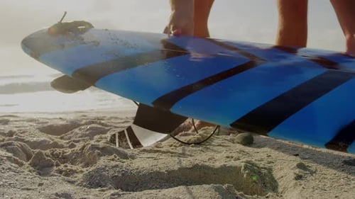 Male surfer picking up surfboard on beach in the sunshine 4k