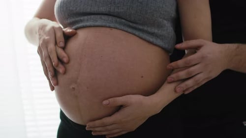 Détail de la mère en cours de grossesse avancée et du futur père touchant l'abdomen. Tourné avec de l'hélium RED