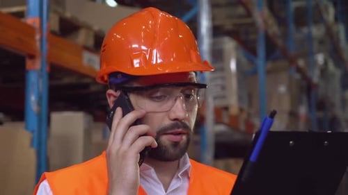 Warehouse worker talking on cellphone holding clipboard