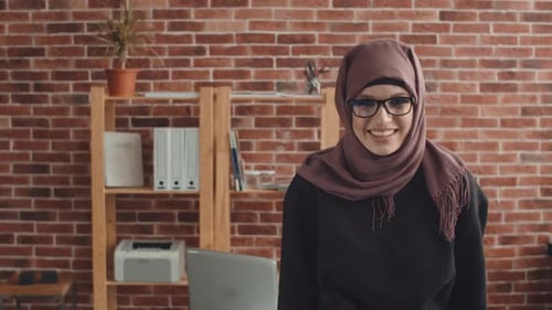 Eine schöne muslimische Frau lacht und lächelt, während sie in die Kamera schaut. Büroangestellter in Hijab