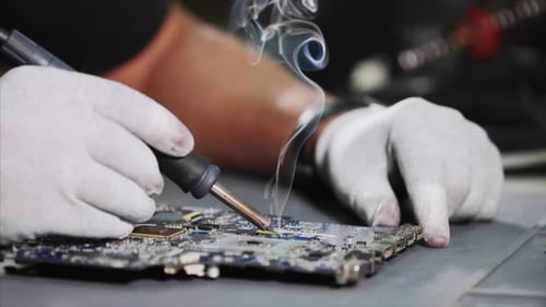 Mechaniker in Handschuhen lötet die Hauptplatine des Computergeräts in der Werkstatt