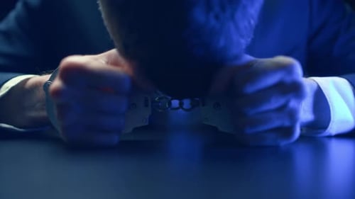 человек в наручниках сидит в комнате для допросов