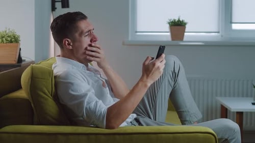 Young Man Relaxing with Smartphone on Couch Indoors