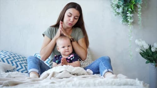 Junge dunkelhaarige Mutter und kleines Mädchen sitzen auf einem Bett und klatschen
