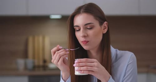 Young Woman Eating Yogurt with Spoon in Kitchen