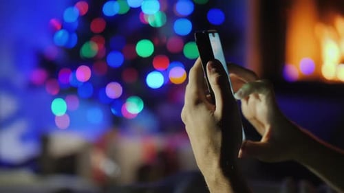 Hands with Smartphone on Blurry Lights of Christmas Tree and Fireplace. Gift Order