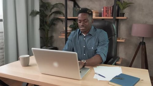 Smiling African Man Employee Works in the Office at the Computer. Black Businessman Looking at