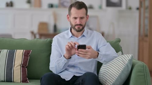 Man Frustrated With Smartphone on Couch Indoors