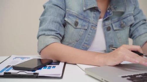 young smiling asian woman working laptop on desk writing notebook document finance at home.