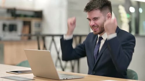Excited Young Businessman Celebrating Success on Laptop in Office