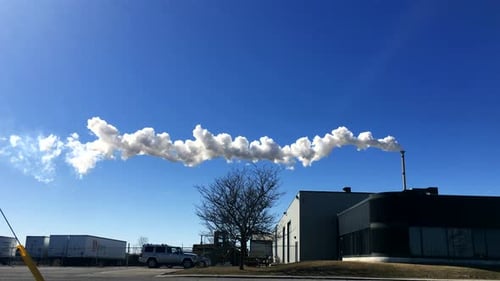 Factory chimney emitting smoke slowly into the sky, panning shot