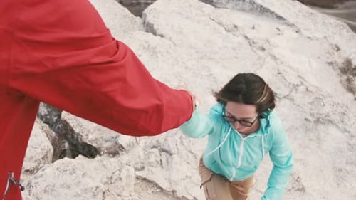 Traveler Man Helps a Woman Climb Up on Top of Rocky Mountain