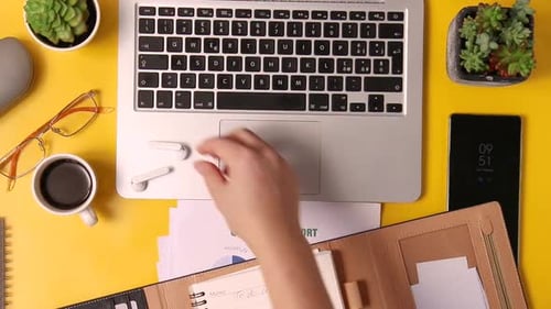 Woman hand put earphones in the case over yellow office desk top view