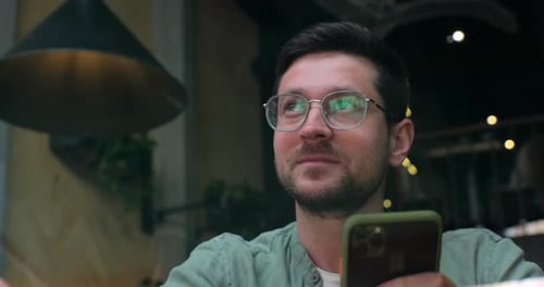 Young Man Sitting in a Cafe and Using Smartphone to Type Sms or Message in Social Media