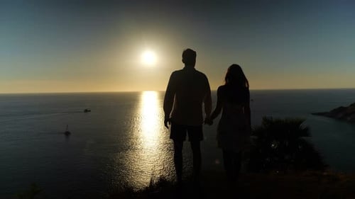 Couple Silhouettes Stand on Beach Edge Admiring Sunset