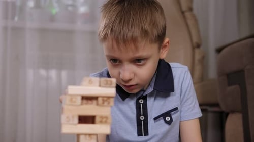 Portrait of a Little Boy Who Takes Out a Wooden Block From a Tower Jenga Game
