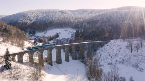 Train de voyageurs traversant un viaduc ferroviaire, chute de neige, de gauche à droite.