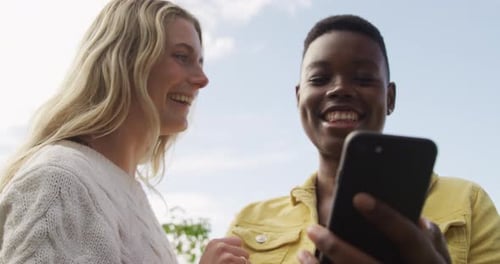 Two Friends Laughing at Phone Outdoors on Sunny Day