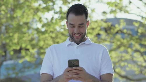 Smiling Young Man Texting on Phone Outdoors