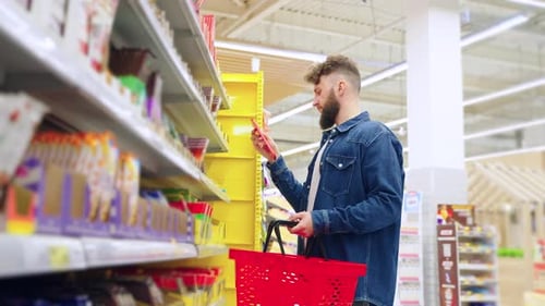 Sweet Department in Supermarket Man is Choosing Chocolate Reading Labels