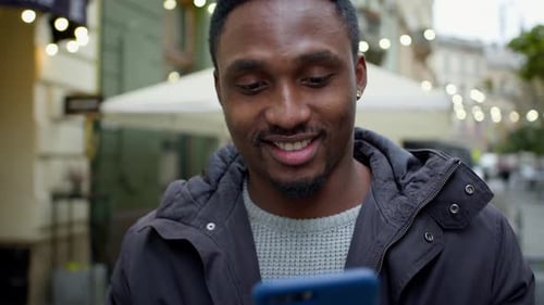 Young Black Guy Walks Down The Street With Phone In His Hands