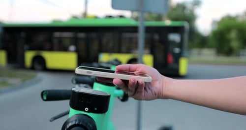 Woman using app on smartphone to unlock electric scooter on the street.