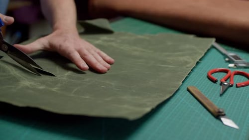 Craftsperson Cutting Green Material With Scissors