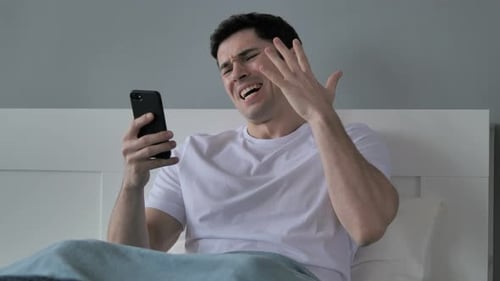Distressed Man Using Smartphone in Bed