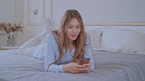 Woman Relaxes on Bed Using Smartphone