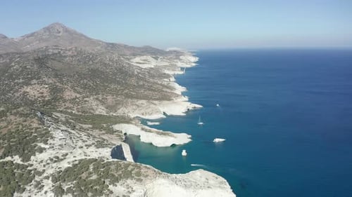 Plataforma rodante aérea ancha frente a la costa con rocas blancas y barcos en el océano