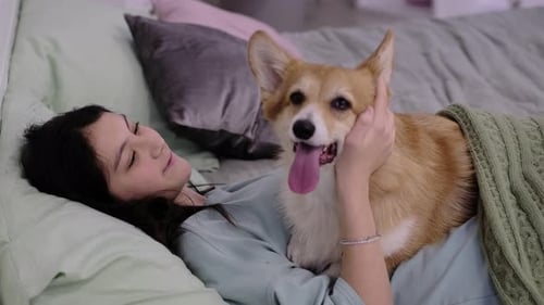Young Woman Cuddles her Corgi Dog on Bed