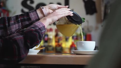 Frauenhand gießt Tee aus Glaskanne in eine Tasse. Tee-Zeit
