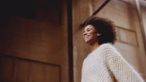 Jovem sorridente com cabelo afro varrido pelo vento andando pela rua