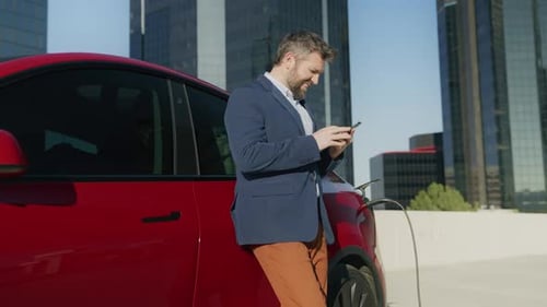 Man Using Phone at Electric Car Charging Station