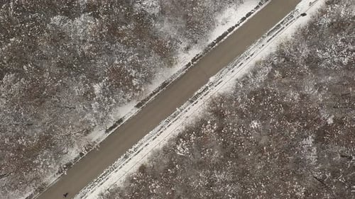 Following unrecognizable pedestrian on road through the snowed forest 4K drone video