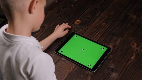 Closeup of a Child Holding a Tablet with a Green Screen on a Wooden Background