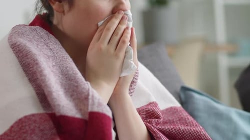 Femme malade assise sur le canapé et toussant dans une serviette