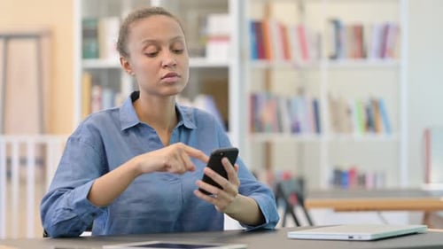Serious African Woman Using Smartphone in Library