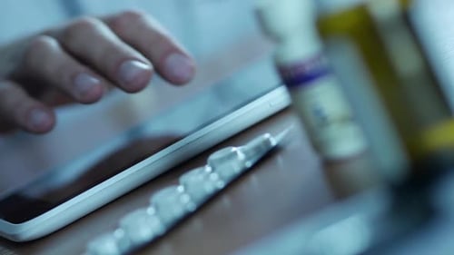 Hand Using Tablet Near Pills and Medicine