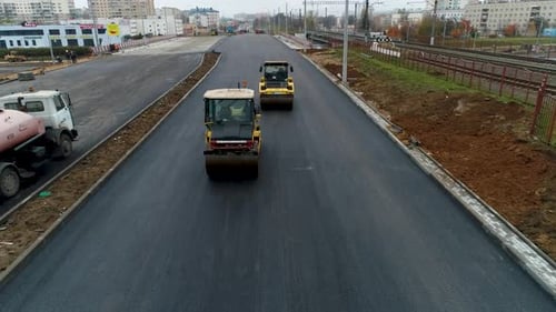 Two Yellow Pavers Ride and Flatten the Hot Asphalt. Steam in Road. Aerial
