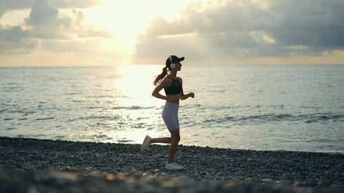 A Young Woman Runner is Listening to Music in Earphones and Training By a Sea