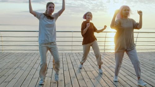 Stylish Young Women Dancing on Pier at Sunrise