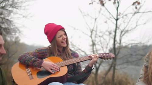 Group of Friends camping.They Are Sitting Around Camp Fire, Playing Guitar