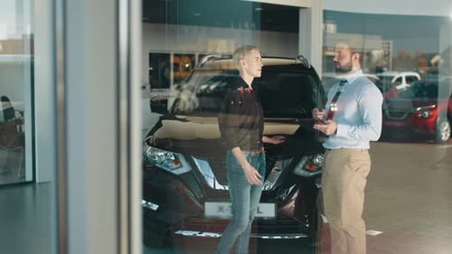 Woman Talks With Car Salesman Inside Dealership Showroom