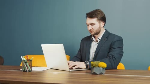 Joven barbudo, programador, apariencia caucásica, sentado y trabajando en un ordenador portátil