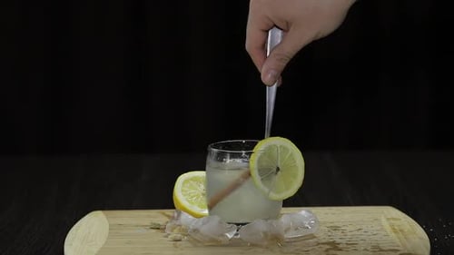Hand Stirring Iced Lemon Cinnamon Beverage on Wood