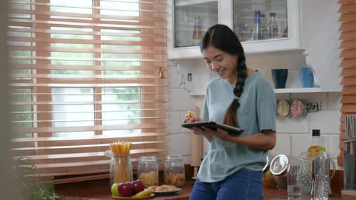 Woman Eats and Uses Tablet in Kitchen
