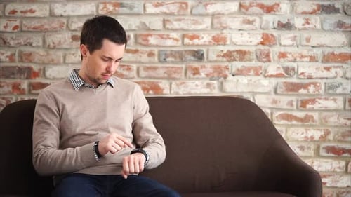 Man Interacting with Smartwatch on Sofa Indoors