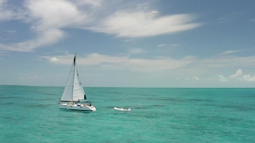Velero con lancha motora conectada en el mar Caribe turquesa, vista aérea de Zumbido