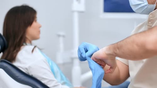 Nahaufnahme Männlicher Zahnarzt zieht bei der Arbeit mit einer Patientin sterile Schutzhandschuhe aus Gummi an